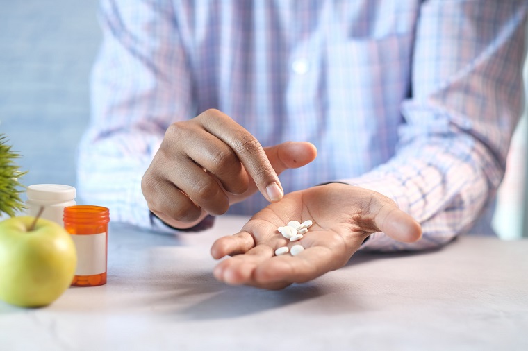 picture of a person holding pills beside an apple and a green plant