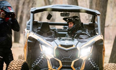 Person in a Can-Am off-road vehicle navigating through a forest trail.